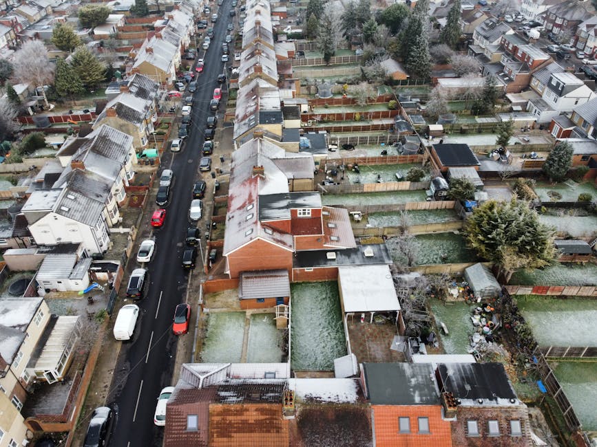 Aerial black-and-white view of a residential neighbourhood showing rows of terraced and semi-detached houses with tiled roofs, front gardens, and parked cars lining the streets. The scene captures a w